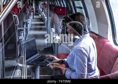 Mujer de negocios sentada en el tren de primera clase, trabajando con un ordenador portátil y un teléfono móvil, Suiza