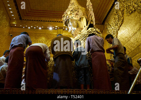 Los hombres aplicando hojas de oro parches al Buda de Mahamuni principal templo del Buda en Mandalay, Myanmar. La hoja de oro es una ofrenda devocional popular. Foto de stock