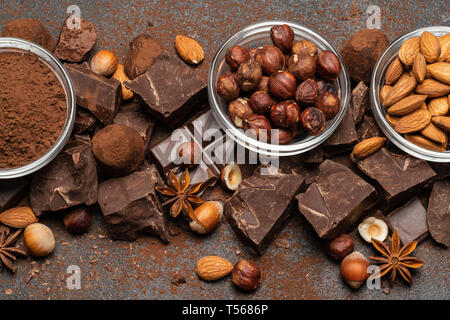 Montón de trozos de chocolate y nueces rotas en el oscuro fondo de hormigón Foto de stock
