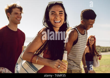 Joven alegre sosteniendo una botella de cerveza caminar al aire libre con amigos. Amigos ir a la playa con bebidas en un día de verano.
