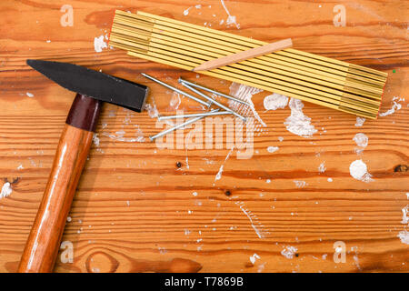 Martillo, regla plegable y uñas sobre un tablero de madera manchada.