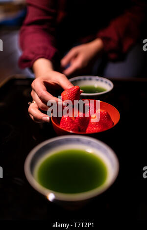 Postre tradicional japonés cuencos tazas con té verde matcha y mujer mano comer fresas en el ryokan con mesa de madera lacada en negro Foto de stock