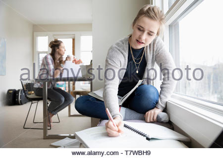 Adolescente haciendo los deberes mientras mamá trabaja en segundo plano.