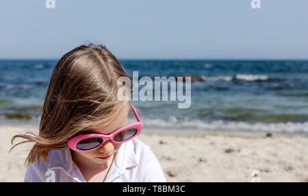 Funny Little Girl (7 años) en gafas de sol se encuentra en la playa. El enfoque selectivo.