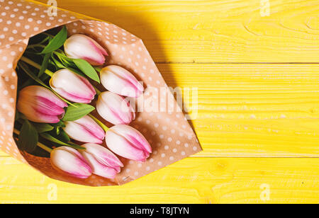  La primavera ya está aquí. Feliz cumpleaños. Ramo de tulipanes rosa fresca sobre amarillo de fondo de la tabla de vista superior. Vacaciones de Primavera saludos. Flores de primavera para el día