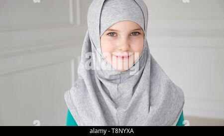Retrato de Muslim 9 años jovencita en gris el hijab es mirando en cámara y riendo. Foto de stock