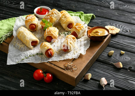 Placa de madera con sabrosos rollitos de salchicha y salsas de mesa de madera Foto de stock
