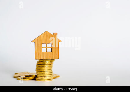 El símbolo de casa está hecha de bambú sobre una pila de monedas de amarillo brillante sobre un fondo claro. Compra inmobiliaria oferta concepto. Copie el espacio.