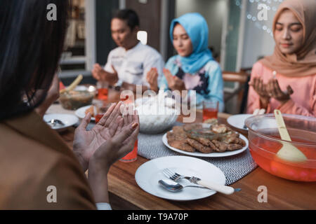 El Hijab mujeres y un hombre orar juntos antes de las comidas, una ruptura rápida comida servida en una mesa en el patio Foto de stock