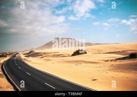 Los viajes en la carretera concepto con largo camino asfaltada en medio de las dunas de arena del desierto y las montañas de aventura y pintoresco lugar alternativo