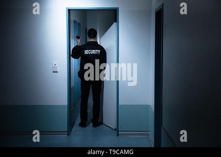 Vista trasera del guardia de seguridad masculino con linterna de pie en el pasillo del edificio Foto de stock