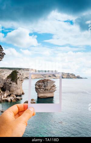 Primer plano de un hombre en los acantilados sobre el mar Mediterráneo en Bonifacio, en Córcega, en Francia, con un marco blanco en su mano el famoso encuadre de grano Foto de stock
