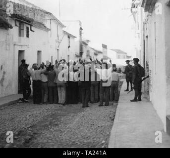Los partidarios del gobierno republicano se aglomeran junto con manos levantadas por soldados españoles en una pequeña calle de un pueblo cercano a Sevilla. Foto de stock