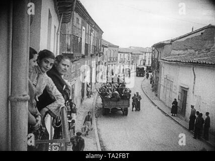 Durante la Guerra Civil Española en 1936, Republicano o español tropas nacionales están cruzando una desconocida aldea española durante la Guerra Civil Española en 1936. Los transeúntes están observando. En primer plano, las mujeres están mirando la cámara desde un balcón. Foto de stock
