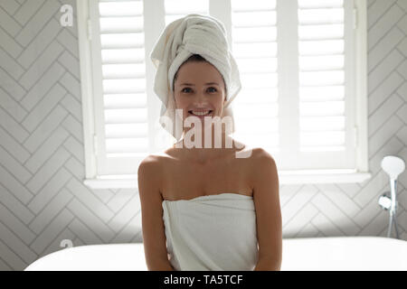 Mujer sonriente sentada en el borde de la bañera en el baño. Foto de stock
