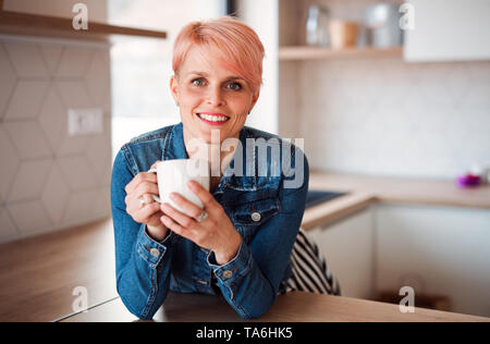 Una joven mujer atractiva recostada sobre un contador en una cocina de casa. Foto de stock