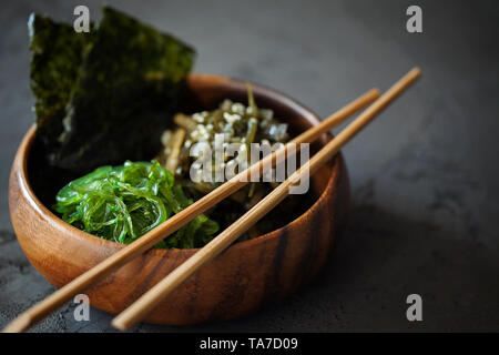 Aperitivo japonés tradicional - Chuka Wakame algas nori tostada crujiente y ensalada de hojas en el tazón de madera sobre fondo oscuro con espacio de copia de texto Foto de stock