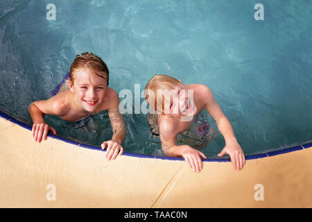 Dos chiquillos felices que son hermanos están sonriendo, mientras nadan en su familia patio piscina en un día de verano.