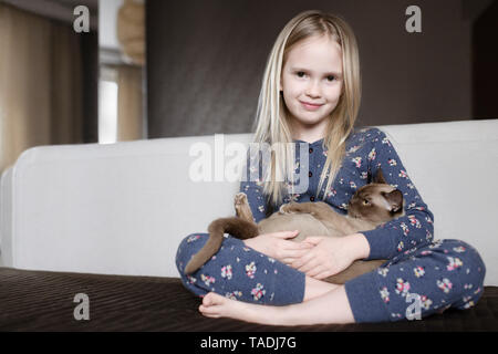Retrato de niña sonriente vistiendo pijama con diseño floral sosteniendo en sus brazos cat