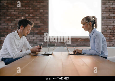 Empresario y una mujer sentada en un escritorio, trabajando con un portátil