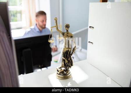 Estatua de la justicia en la estantería y abogado que trabaja en la oficina a fondo