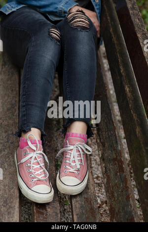 Mujer jeans negros rasgados y sneakers de lona rosa sentado solo un banco del parque Fotografía de stock - Alamy