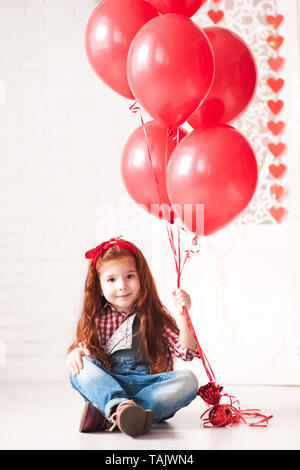 Lindo bebé niña 3-4 años de la celebración de los globos rojos sentados en  el piso n white room. Mirando a la cámara. Fiesta de cumpleaños Fotografía  de stock - Alamy