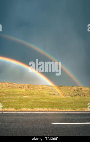 Arco iris sobre la carretera con las nubes en el cielo, cielo oscuro, lluvioso en el exterior. Rainbow y tormenta al mismo tiempo