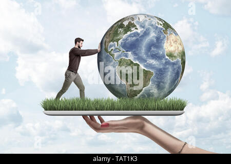 Vista lateral de la cosecha de la mano que sostiene la mujer tableta digital con hierba verde creciendo en pantalla y poco hombre empujando el planeta Tierra en la parte superior. Foto de stock
