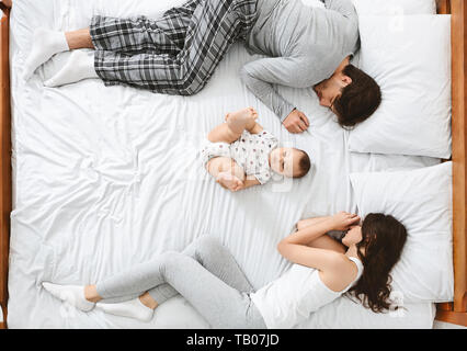 Poco bebé acostado en el centro de la cama, los padres durmiendo en lados