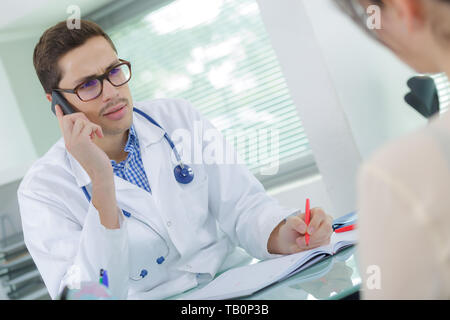 Doctor utilizando teléfono mientras en consulta con el paciente