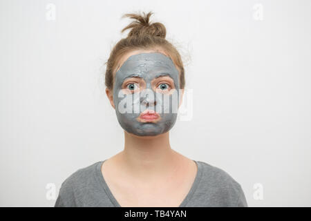 Joven mujer caucásica con negro o gris arcilla facial máscara sobre su cara divertida Foto de stock