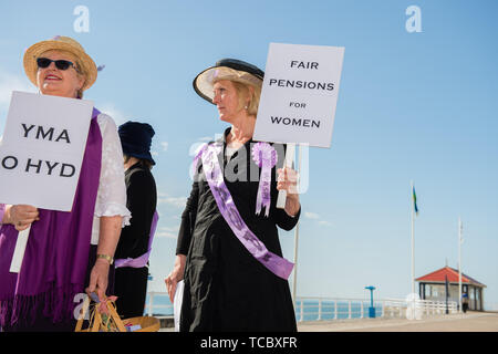 Gales Aberystwyth, Reino Unido Jueves 06 de junio de 2019 un grupo de abuelas portadoras de etiqueta en sus 60s, vestido como suffragettes marchando por el paseo marítimo en Aberystwyth como parte de un programa nacional de protesta contra el aumento de la edad de jubilación estatal mujeres . [Mujer WASPI Pensión estatal contra la injusticia] están haciendo campaña para revertir la decisión de modificar la edad de jubilación a los 67 años para las mujeres nacidas en los años 1950 . Hay 5.000 mujeres en Ceredigion nacido en 1950 que han perdido años de sus pensiones como consecuencia de la política de aceleración del gobierno. La legalidad de estos cambios es que se están probando actualmente. Foto de stock