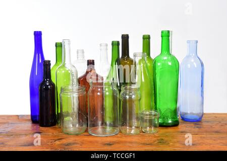 Grupo de botellas y frascos de vidrio sobre una mesa de madera con fondo blanco.