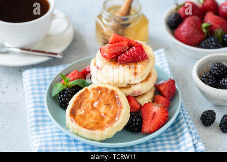 Requesón tortitas syrniki con fresa, zarzamora y miel sobre placa azul. Sabroso desayuno saludable Foto de stock