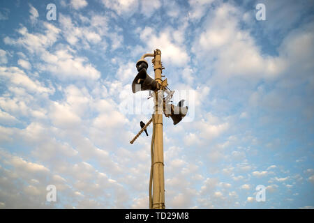 Cerca de dos megáfonos exterior en la pole con dos pájaros negros contra el azul cielo nublado. Dos altavoces con polvo de aspecto antiguo en el poste. Conexión Foto de stock