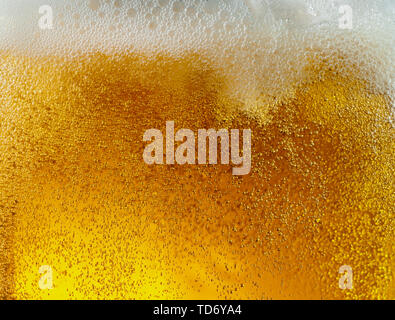 Vista cercana de burbujas flotando en la luz de fondo de color dorado de la cerveza. Textura de refrigeración del verano beber filtrada con espuma y macro fizz en la pared de cristal. Efervescentes o flotando en la parte superior de la superficie. Foto de stock