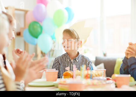 Retrato de niño sonriente vistiendo crown sentado en la tabla mientras celebrando un cumpleaños con amigos, espacio de copia