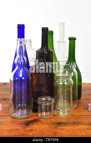 Grupo de botellas y frascos de vidrio sobre una mesa de madera con fondo blanco.