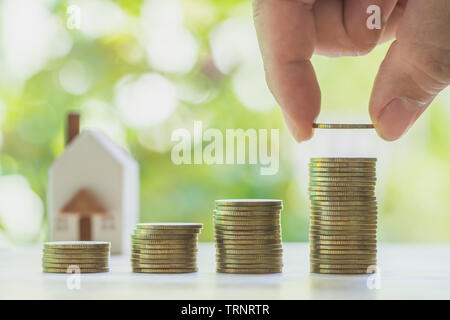 Casa u hogar modelo en cerca de monedas pila. Concepto de préstamo, escalera de propiedad, financiera, hipoteca, inversión inmobiliaria, impuestos y bonus.