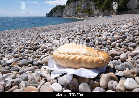 Cornish pasty en playa de guijarros con mar de fondo Foto de stock