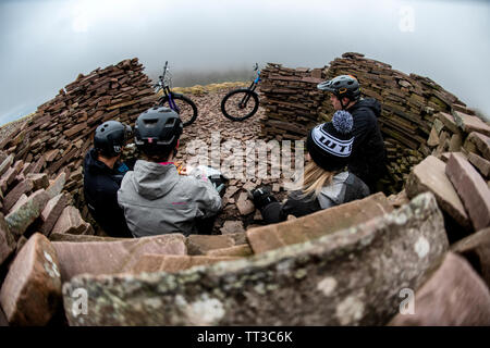 Un grupo de ciclistas de montaña detener al abrigo de las inclemencias meteorológicas en el mojón, cerca de la Cumbre y del ventilador grande en Brecon Beacons, Gales. Foto de stock
