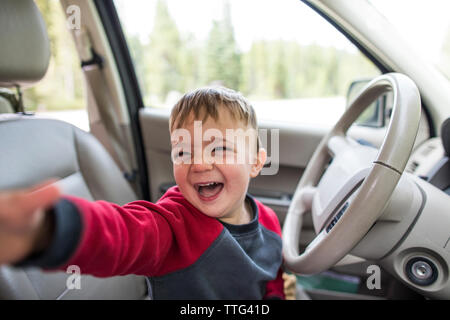 Poco feliz muchacho sentado en el asiento del conductor de un coche Foto de stock