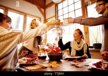 Amigos elevando brindis de celebración a la mesa en casa Foto de stock