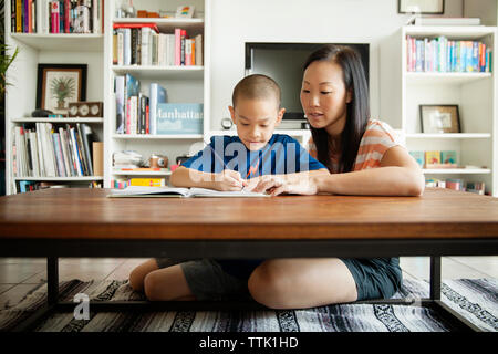 Mujer ayudando a su hijo en estudiar mientras están sentados en el piso en casa