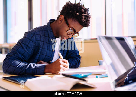 Hombre escribir mientras está sentado a la mesa en la biblioteca