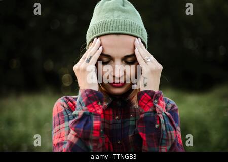 Mujer joven con la cabeza entre las manos de pie en campo