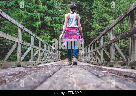 Vista trasera de la mujer caminar sobre la pasarela en medio de los árboles en el bosque