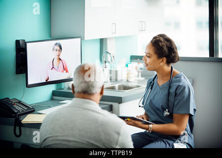 Doctora discutiendo con colega en conferencia telefónica mientras está sentado con la paciente en la clínica Foto de stock