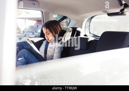 Chico serio libro de lectura mientras está sentado en el coche visto a través de la ventana